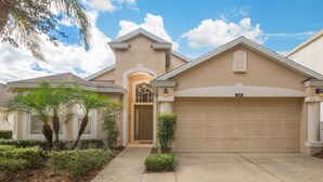 A residential house with a beige facade, a garage, and a well-maintained front yard with palm trees and shrubs. - The Hamlet at Westhaven 320 (Davenport)