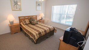 Ein Schlafzimmer mit einem Bett, zwei Nachttischlampen, einem Deckenventilator, einem Fenster mit Jalousien und einem Fernseher auf einem Schrank.