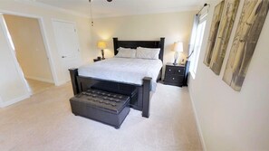 A bedroom with a bed, two bedside tables, a bench, a door, and a wall with a curtain. - Paradise Palms 8876 (Kissimmee)
