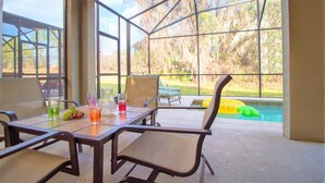 A covered patio with a table and chairs, a pool, and a view of trees. - Paradise Palms 8876 (Kissimmee)