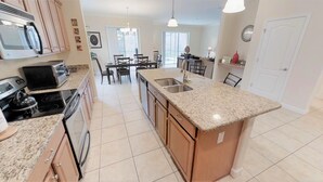 A modern kitchen with granite countertops, a built-in oven, and a dining area with a table and chairs. - Paradise Palms 8876 (Kissimmee)