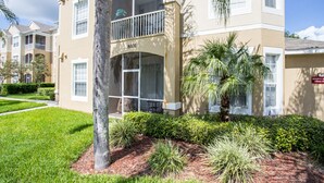 A multi-story building with a balcony on the second floor, surrounded by well-maintained landscaping including palm trees and shrubs. - Windsor Palms Condos 8101 - 105 (Kissimmee)