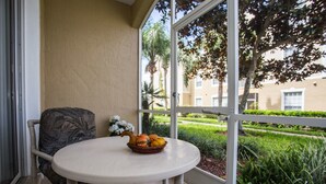 A small round table with a basket of fruit on a balcony with a view of a garden and buildings. - Windsor Palms Condos 8101 - 105 (Kissimmee)