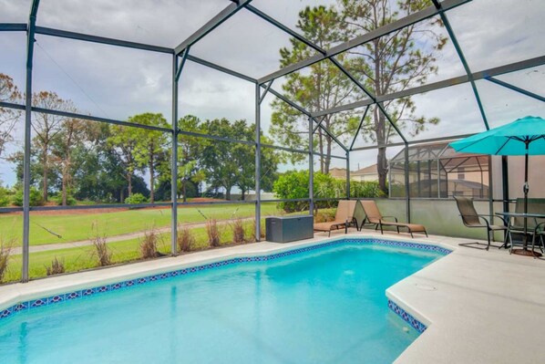 A swimming pool with a glass enclosure, surrounded by lounge chairs and a table with a blue umbrella.