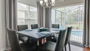 Un coin repas avec une table dressée pour six personnes, un lustre et une vue sur une piscine.