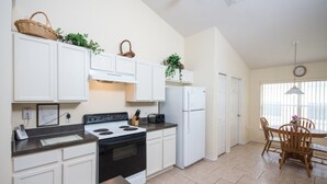 Una cocina con armarios blancos, estufa, refrigerador y un comedor con mesa y sillas.