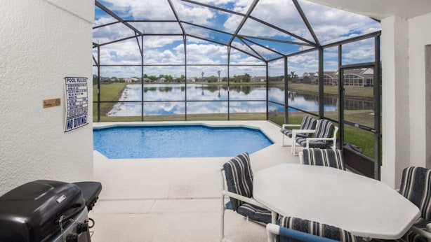 Un área de piscina con vista a un lago, una parrilla y una mesa con sillas.