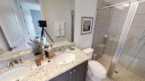 A modern bathroom with a granite countertop, two sinks, a toilet, and a glass shower enclosure. - Encore Resort at Reunion 430 (Kissimmee)