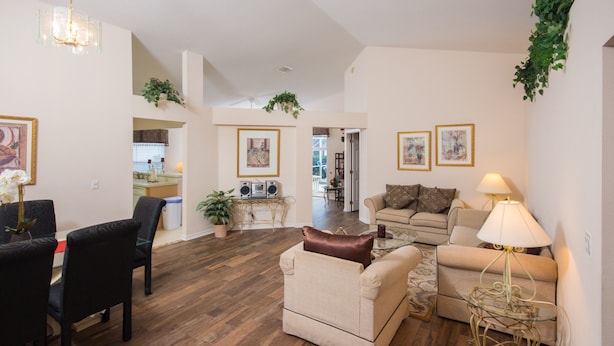 A spacious living room with a wooden floor, a sofa set, a coffee table, and a lamp. There are framed pictures on the walls and a chandelier hanging from the ceiling. - Highlands Reserve Golf & Country Club 104 (Davenport)
