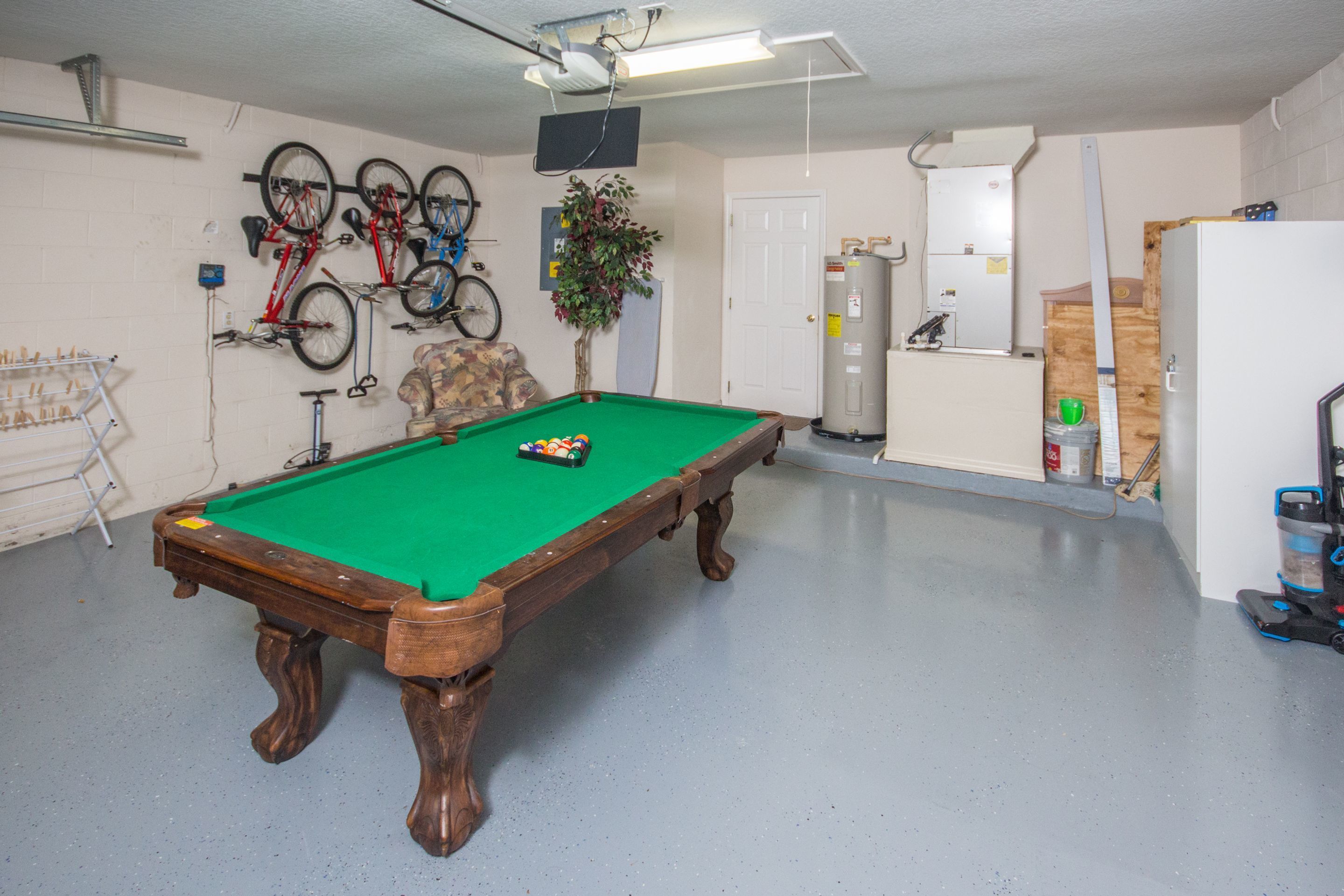 Une table de billard dans une pièce où sont accrochés des vélos au mur, ainsi qu’une plante et un réfrigérateur.