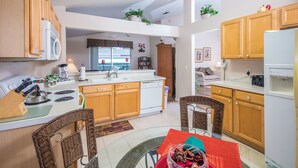 A spacious kitchen with wooden cabinets, a central island, and a dining area with wicker chairs. - Highlands Reserve Golf & Country Club 104 (Davenport)