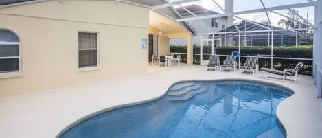 Una piscina interior con techo de vidrio, rodeada de sillones de descanso y un edificio color beige.