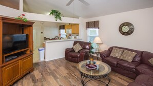 A living room with a TV, leather chairs, a glass coffee table, and a kitchen in the background. - Highlands Reserve Golf & Country Club 104 (Davenport)