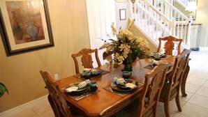 Uma sala de jantar com uma mesa de madeira posta para seis pessoas, rodeada por cadeiras. Há um vaso com flores sobre a mesa.
