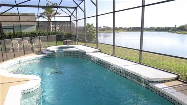 Piscina com design curvo, rodeada por um revestimento de vidro, e vista para um lago.