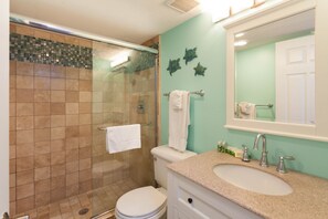 Une salle de bain avec une douche à parois de verre, des toilettes blanches, un lavabo avec un miroir au-dessus et des décorations murales représentant des tortues.