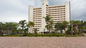 A multi-story hotel with a central courtyard, palm trees, and a paved walkway.