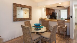 A dining area with a round glass table, four wicker chairs, and a blue bowl centerpiece.