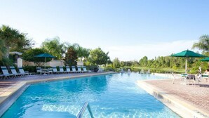 Une piscine à l’eau d’un bleu cristallin, entourée de chaises longues et de parasols, et un chemin piétonnier pavé de briques.
