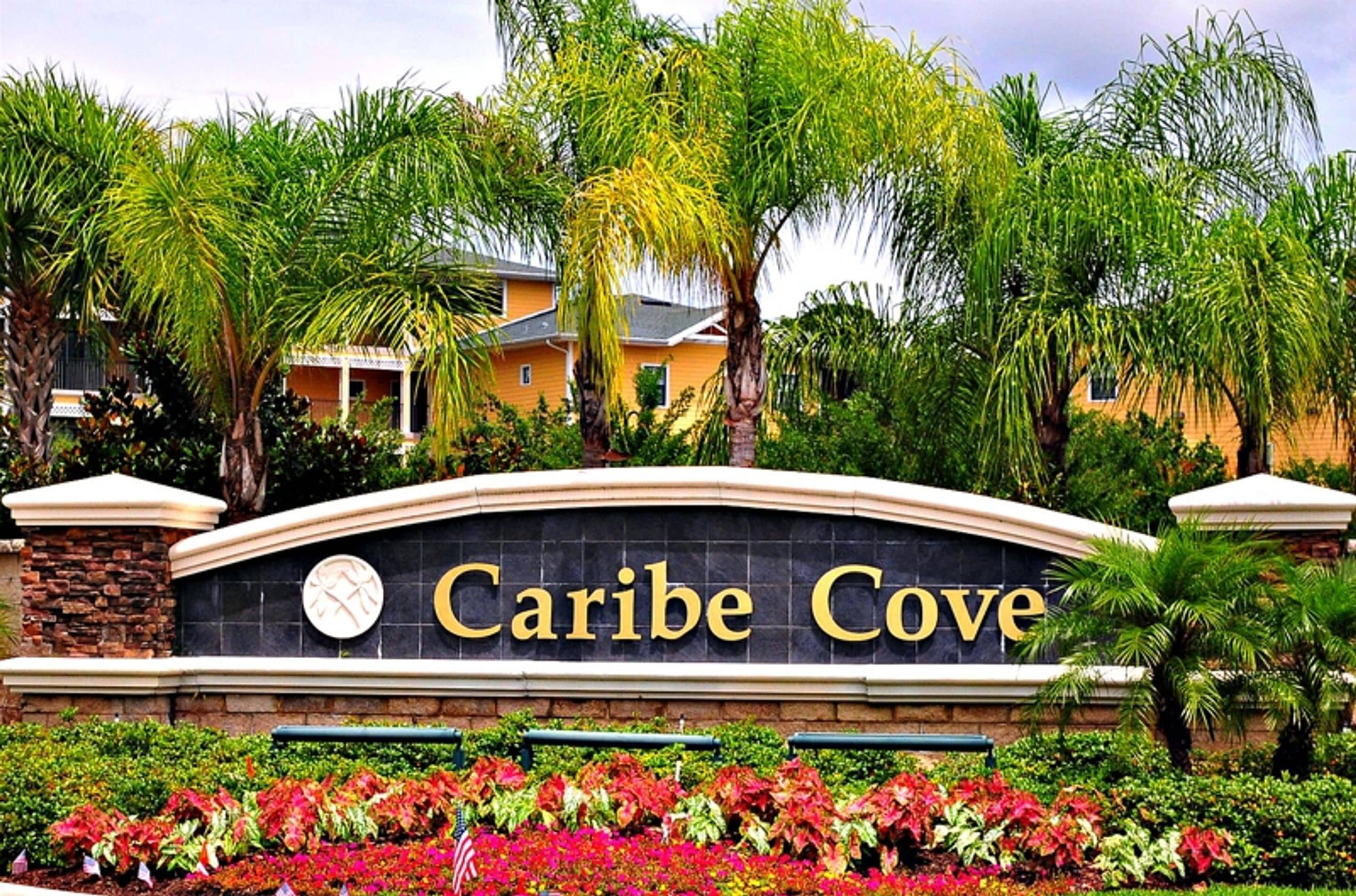 A sign for "Caribe Cove" with a stone arch and a clock, surrounded by lush greenery and palm trees.