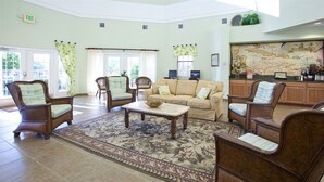 Un hall d’entrée spacieux, avec un canapé beige, des fauteuils en bois, une table basse et une grande carte accrochée au mur.