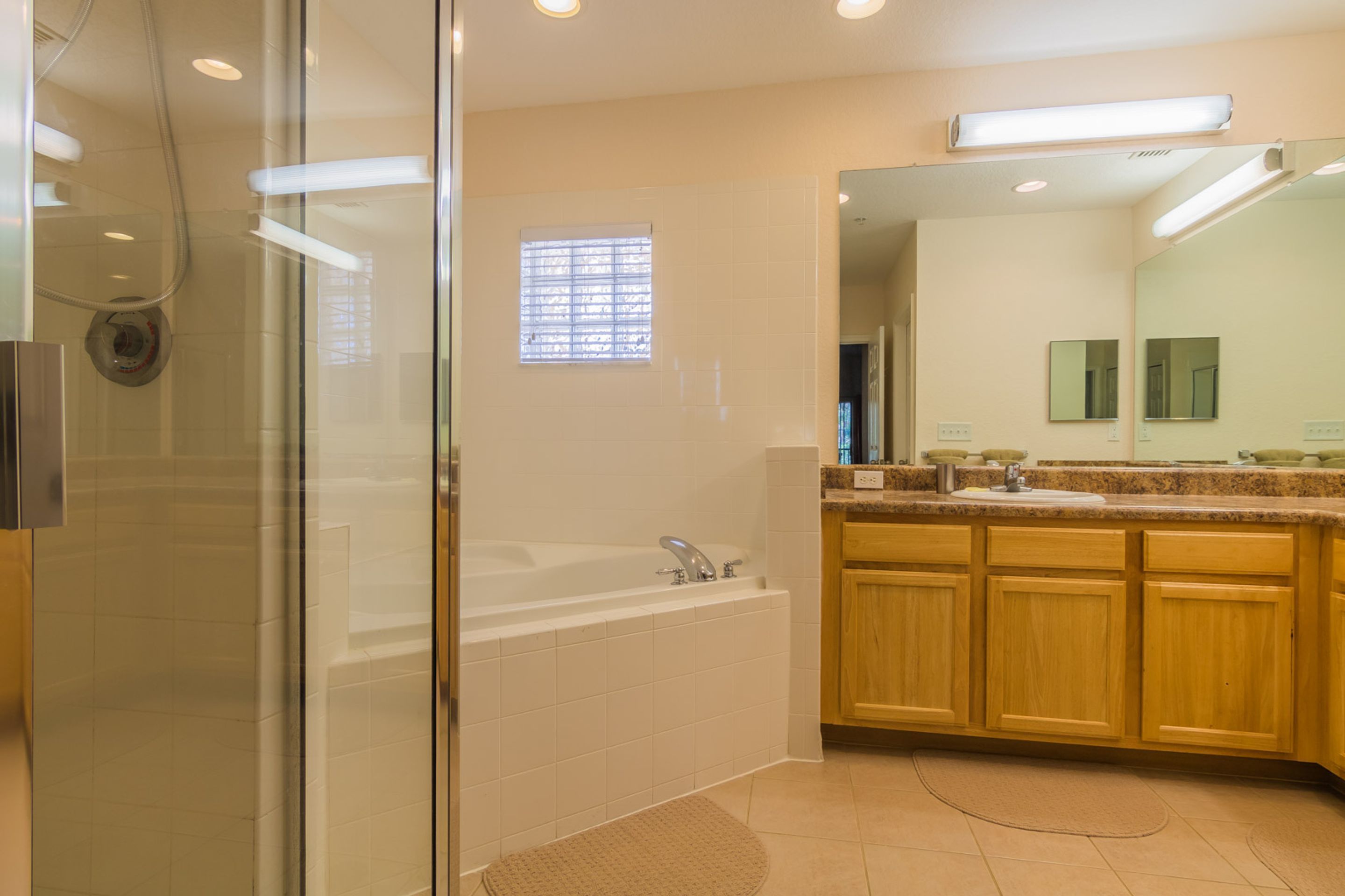 A modern bathroom with a glass shower enclosure, a bathtub, wooden cabinets, and a large mirror.