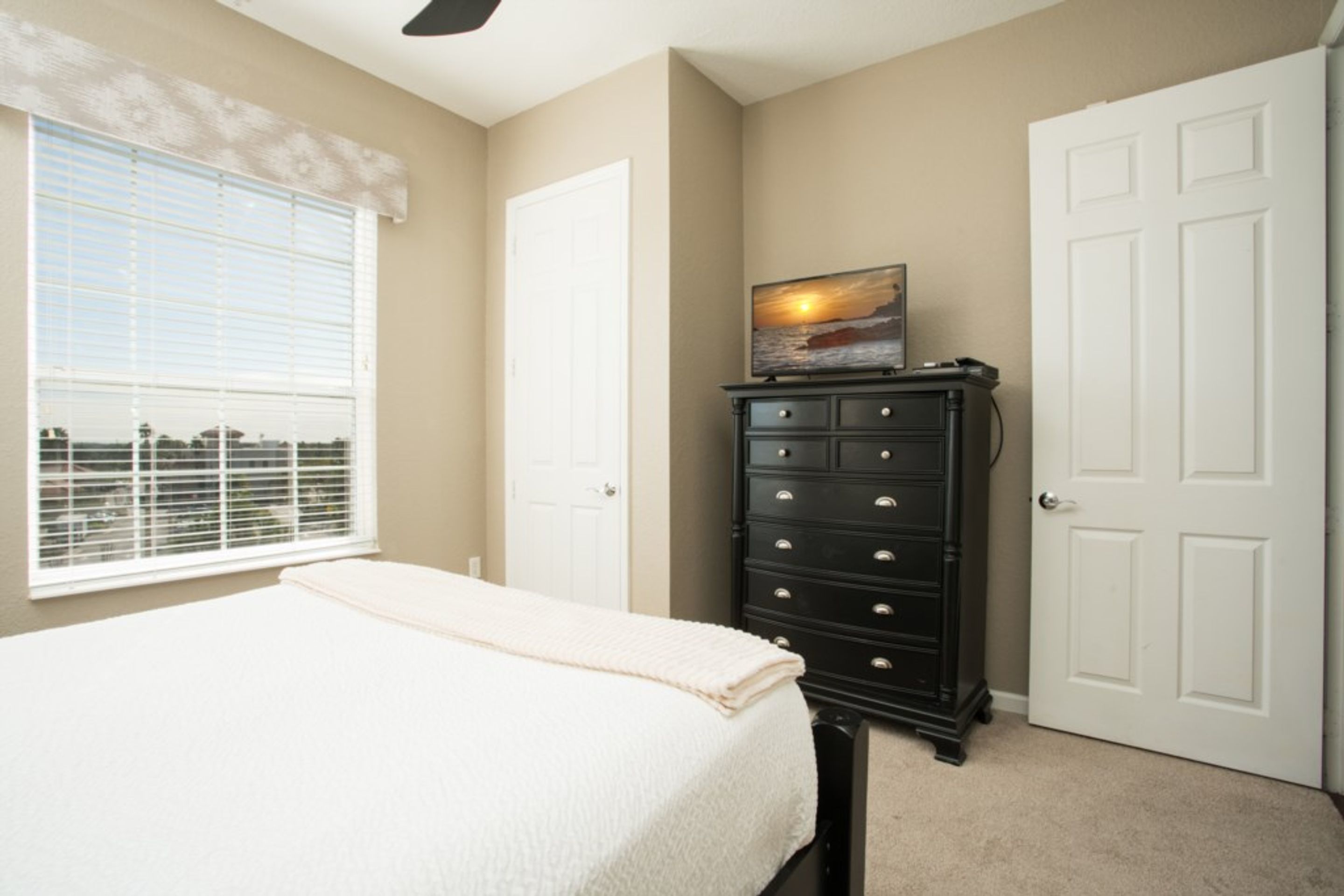 A bedroom with a bed, a dresser, and a window with blinds.