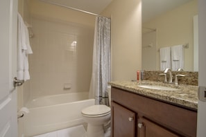 A bathroom with a bathtub, toilet, and vanity with a sink and mirror. - Champions Gate 9027 A (Davenport)
