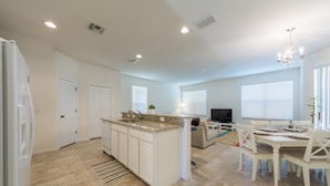A spacious kitchen with a central island, a dining area with white chairs, and a living room with a sofa and TV. - Bella Vida 871 (Kissimmee)