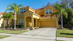 A yellow two-story house with a red-tiled roof, a front porch, and a garage. - Bella Vida 871 (Kissimmee)