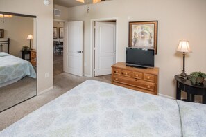 A bedroom with a bed, dresser, TV, and a door leading to a hallway.