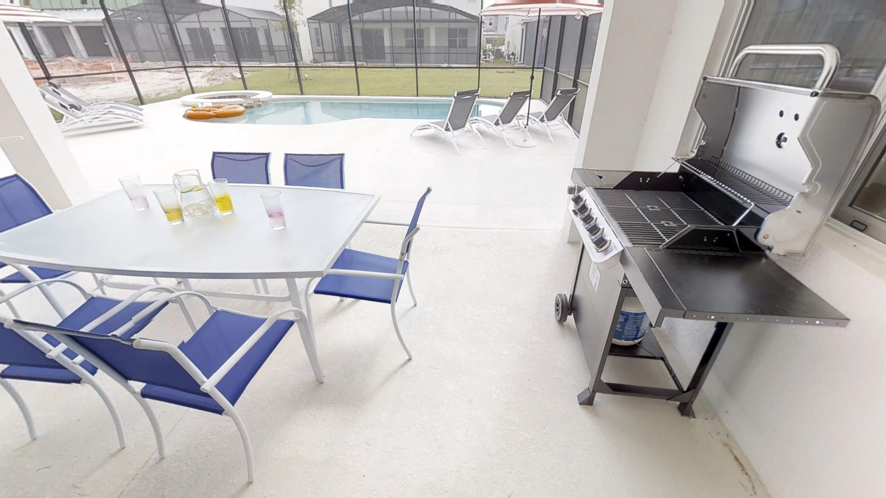 A patio area with a pool, a barbecue grill, and a table with chairs.