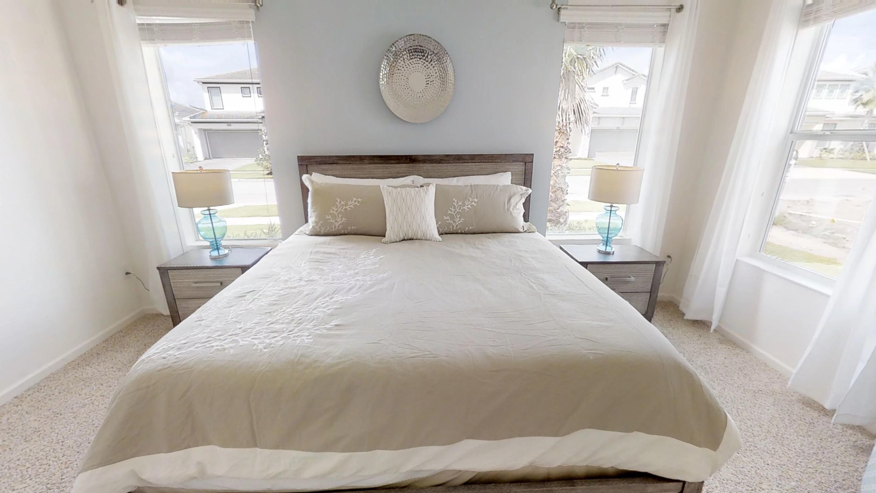 Une chambre avec un grand lit, deux tables de chevet avec des lampes, un élément décoratif mural et une vue sur l’extérieur.