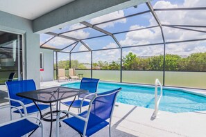 A pool area with blue chairs and a table, a glass enclosure, and a view of greenery. - Hillcrest Estate 532 (Davenport)