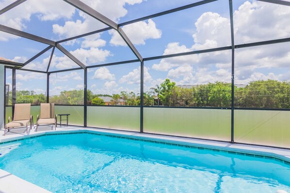 Une piscine entourée de parois en verre, avec des chaises et une vue sur les arbres et les bâtiments.