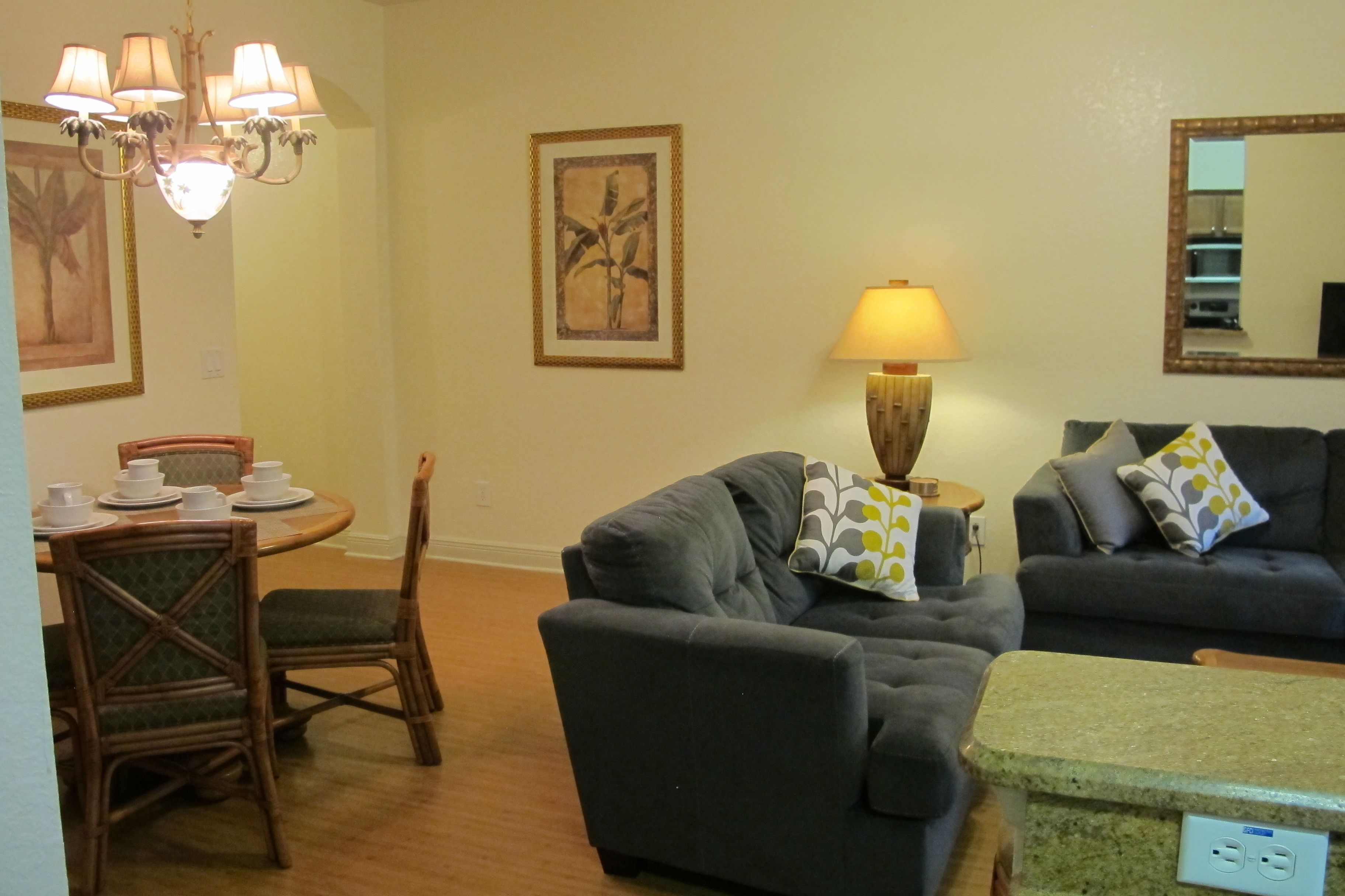 A living room with a grey sofa, a dining table set with white plates and cups, a chandelier, and a lamp.