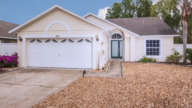 Une maison de plain-pied avec un garage blanc, une porte d’entrée verte et une allée menant à l’entrée.