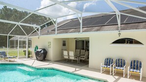 Un espace piscine extérieur abrité, doté de chaises longues, d’un barbecue et d’une table de patio.