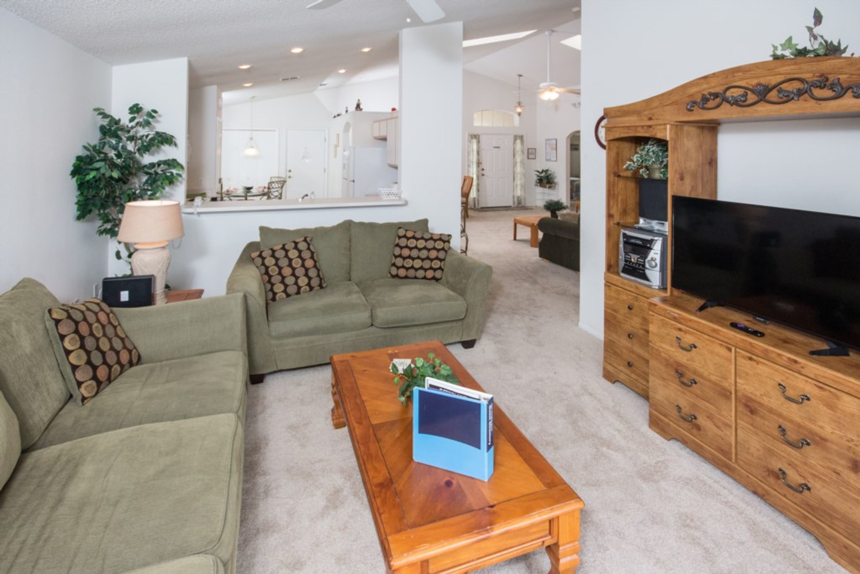 A living room with a sofa, coffee table, TV stand, and a dining area in the background.