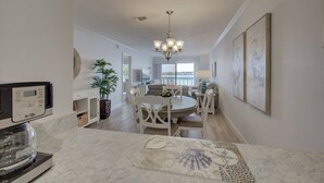 A modern kitchen with a coffee maker, a dining area with a chandelier, and a view of the living room. - Anna Maria Island 1301 2B (Bradenton Beach)