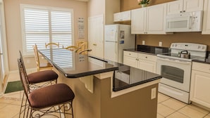 A kitchen with white cabinets, a black countertop, a stove, and a refrigerator. - Windsor Palms 2200 (Kissimmee)