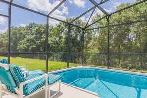 A swimming pool with a glass enclosure, surrounded by a black fence and trees in the background.
