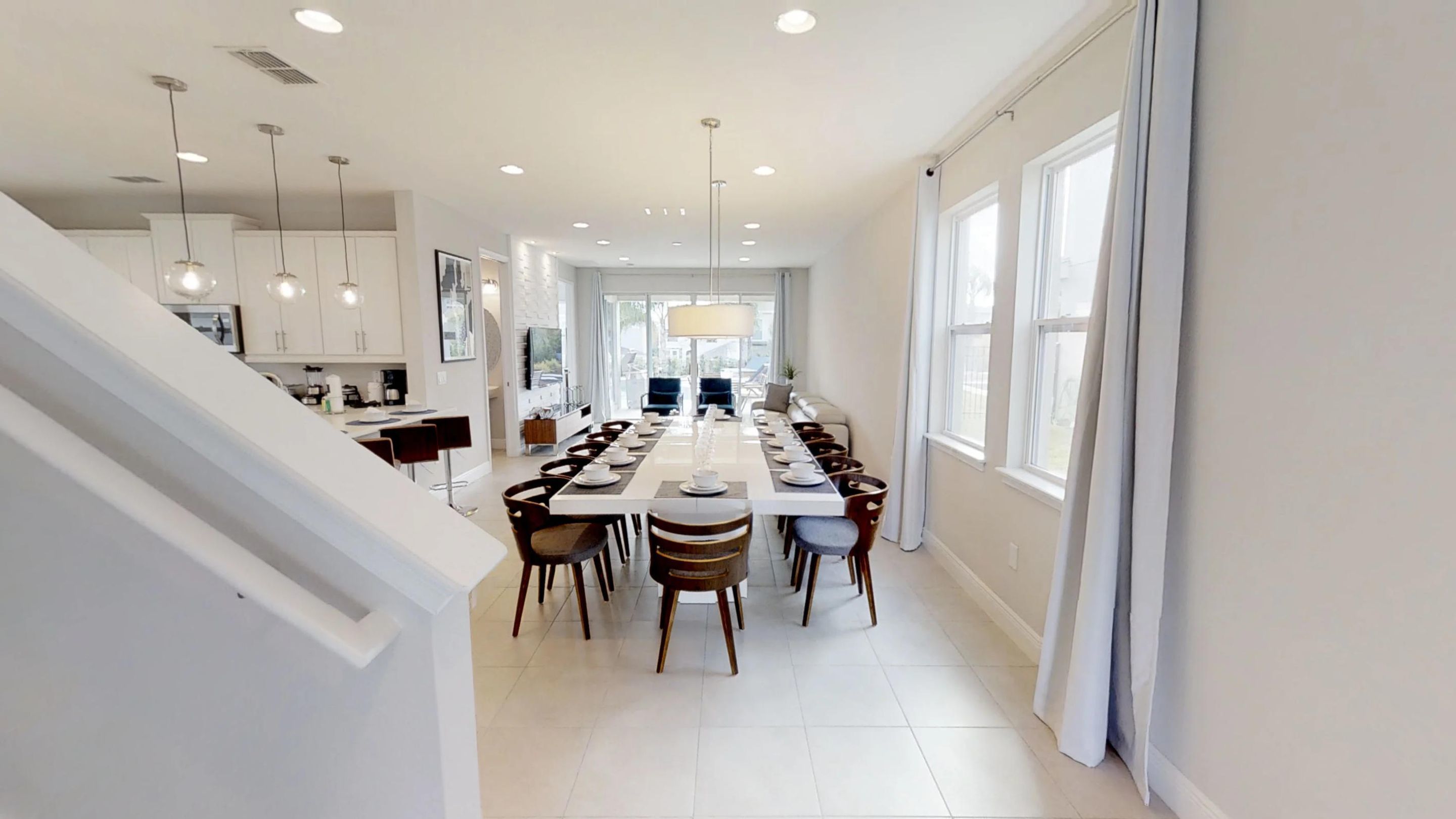 A modern kitchen with white cabinets, a dining area with a long table, and a staircase leading to an upper level.