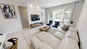 A modern living room with a large sofa, a coffee table, a TV, and a dining area with a table and chairs.
