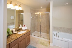 Une salle de bain avec un lavabo surmonté d’un plan de travail en granit, une douche à parois de verre et une baignoire blanche.