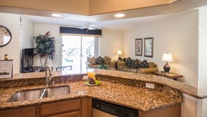 A kitchen with granite countertops, a dishwasher, and a sink. There is a dining area with a sofa and a lamp.