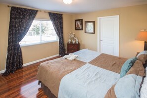 A bedroom with a large bed, wooden flooring, a window with curtains, a dresser, and a lamp. - Windsor Hills 2591 (Kissimmee)