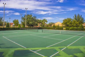 A tennis court with net, surrounded by trees and buildings. - Windsor Hills 2591 (Kissimmee)