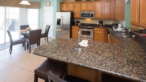A kitchen with granite countertops, wooden cabinets, stainless steel appliances, and a dining area with a table and chairs. - Windsor Hills 2591 (Kissimmee)