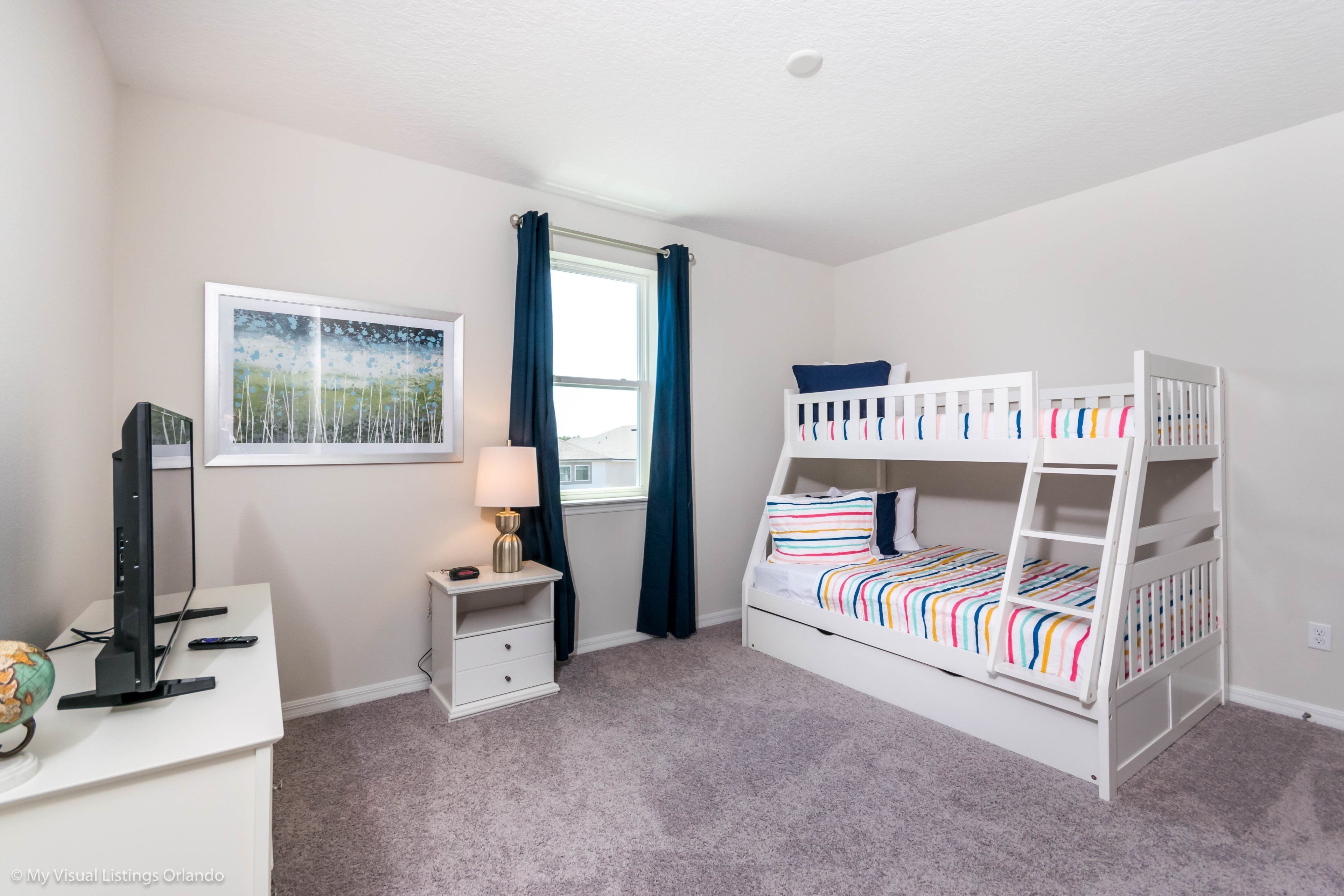 A bedroom with bunk beds, a desk with a computer, a lamp, and a window with curtains.